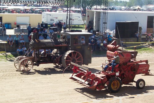 Antique steam engine and antique tractor parading before grandstand area . . .